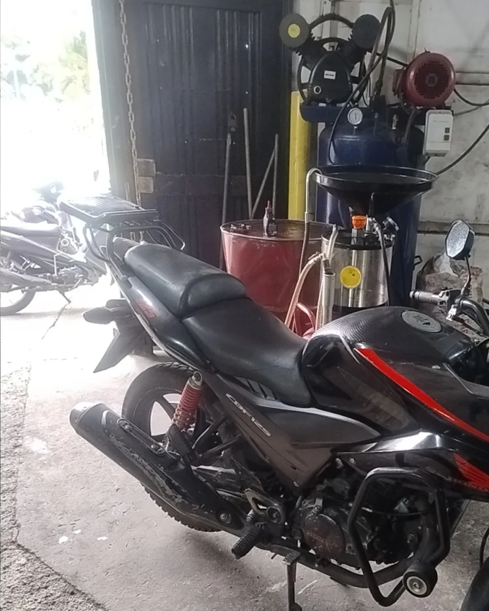 Moto parqueada dentro del taller, junto al compresor y el recolector de aceite